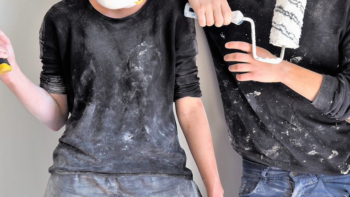 Homeowners in overalls holding a sledgehammer and paint roller while renovating a room
